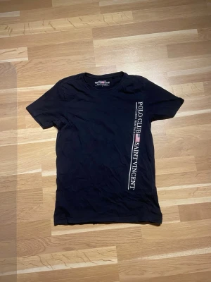 Schysst T-shirt från polo club - Mörkblå T-shirt från Polo Club Saint Vincent i storlek S. T-shirten har ett stilrent tryck med Polo Club-loggan och amerikanska flaggan. En klassisk och enkel modell som passar till det mesta. Använd men i fint skick, säljs då den inte längre kommer till användning.