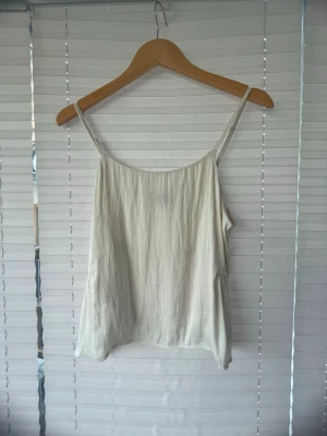 Beige linnetopp med tunna axelband - Sitter ej som en m utan S!Säljer en ljusbeige linnetopp med tunna axelband och avslappnad passform. Toppen har en enkel, flowy design och är tillverkad i ett mjukt material som känns svalt mot huden. Perfekt för varma dagar och enkel att styla med olika outfits. Är lite sönder vid ena bandet men syns ej mycket 