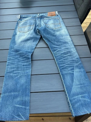 Blå raka jeans med slitningar - Säljer ett par klassiska blå jeans från Ralph lauren med lite åt de slimare hållet och tydliga slitningar. Jeansen har fem fickor, ljus tvätt och kontrastsömmar. Materialet är denim i bomull och passformen är avslappnad. Perfekta för en avslappnad och trendig look. 