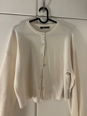 Vit basic kofta med knappar - Klassisk vit kofta med rund halsringning och knäppning framtill. Tröjan har långa ärmar och ribbade muddar vid ärmslut och nederkant. Perfekt att slänga över en topp för en clean look.
