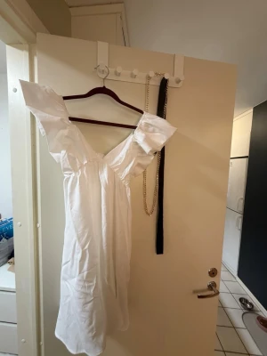 Vit kort klänning med volangärm - Söt vit kort klänning med stora volangärmar och v-ringning. Klänningen har en omlottknytning framtill och är tillverkad i ett lätt tyg, perfekt för varma dagar. Passformen är normal och modellen är luftig och feminin.