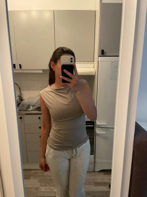 Beige ärmlös topp i bomull - En enkel och stilren beige topp i mjuk bomull. Modellen är ärmlös med rund halsringning och har en rak passform som sitter snyggt på kroppen. Perfekt att matcha med jeans eller kjol för en clean look.