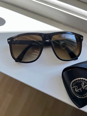 RayBan Boyfriend  - Snygga svarta solglasögon från Ray-Ban med klassisk Wayfarer-form och bruna tonade glas. Bågarna är i plast och har diskret Ray-Ban-logga på sidan. Perfekta för soliga dagar och ger en cool vibe till din outfit.