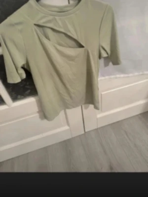 Ljusgrön topp med cut out-detalj - Trendig ljusgrön topp med unik cut out-detalj vid halsen. Kortärmad och i mjukt material, perfekt för dig som vill sticka ut lite extra. Passar snyggt till både jeans och kjol.Fin topp med slits vid bröstet, knappt använd st.XL Tajt i modelen