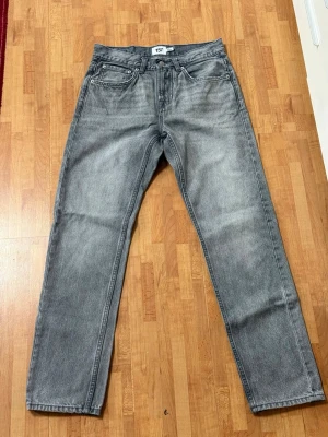 Grå raka jeans med fem fickor - Säljer ett par grå jeans med rak passform och klassisk femficksdesign. Jeansen har en snygg tvättad look och silverfärgade nitar. Perfekta för dig som gillar en avslappnad och stilren stil.
