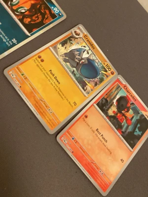 Pokémonkort: Chi-Yu, Cranidos, Charcadet - Tre Pokémonkort säljes: Chi-Yu (blått kort med fiskmotiv), Cranidos (orange kort med dinosauriemotiv) och Charcadet (orange/rött kort med eldtema). Perfekt för samlare eller dig som vill utöka din kortlek. Alla kort har färgstarka illustrationer och tydliga attacker.