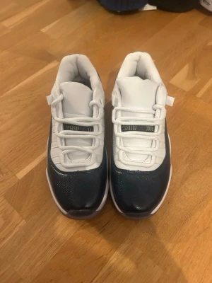 Vita och marinblå sneakers - Snygga sneakers i vitt och marinblått med lågt skaft och coola detaljer. Ovandelen är i en mix av slätt och glansigt material, med vita skosnören och en tydlig kontrast mellan färgerna. Perfekta för dig som vill ha en clean och sportig look.