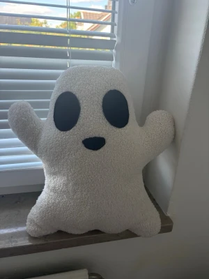 Vit spökformad kudde - Mysig kudde i form av ett spöke med vit fluffig yta och svarta detaljer för ögon och mun. Kudden har en lekfull design och passar perfekt som dekoration till halloween eller för att skapa en rolig stämning i rummet.