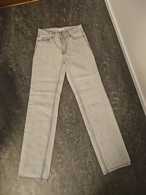 Jeans från Gina Tricot  - Säljer ett par ljusgrå jeans med rak passform och klassisk femficksdesign. Jeansen har hög midja och är tillverkade i ett mjukt denimtyg som ger en avslappnad look. Perfekta för dig som gillar en enkel och stilren stil. 