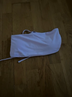 Ljuslila bandeau bikiniöverdel - Säljer en ljuslila bandeau bikiniöverdel med snörning i ryggen för justerbar passform. Enkel och stilren design utan mönster, perfekt för sommardagar på stranden eller vid poolen.