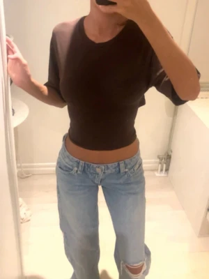 Brun croppad topp med knyt i ryggen - Säljer en brun croppad topp med korta ärmar och snygg knytning i ryggen. Toppen har en tight passform och är perfekt till jeans eller kjol. Materialet känns mjukt och stretchigt, troligen bomull eller polyester.