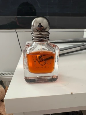 Strong You Intensely parfym - En elegant parfymflaska med rundad silverfärgad kork och tjockt glas. Vätskan inuti är bärnstensfärgad och flaskan har texten 'Strong You Intensely' på framsidan. Perfekt för dig som gillar intensiva dofter och snygg design.