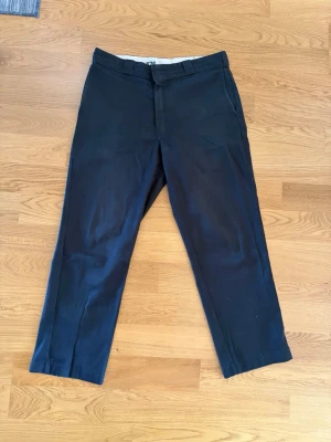 Svarta chinos från Dickies - Snygga mörkblå chinos från Dickies med klassisk rak passform och bälteshällor. Byxorna har två sidofickor fram och två bakfickor, varav en med knapp. Tillverkade i slitstarkt material som passar perfekt till en avslappnad stil. Storlek: 32/32. 