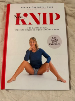 Nya Knip av Karin Björkegren Jones - Boken 'Nya Knip' av Karin Björkegren Jones har hårda pärmar med vit och röd design. Den handlar om bäckenbottenträning för bättre sexliv, hållning och starkare kropp. Omslaget visar en kvinna i blå tröja och randiga shorts. Perfekt för dig som vill lära känna ditt underliv.