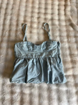 Ljusblå bustier topp med volang - Supersöt ljusblå bustier topp med tunna axelband som går att ta av. Toppen har markerade kupor och en volangig, luftig nederdel. Perfekt för sommaren och ger en trendig look till jeans eller kjol.