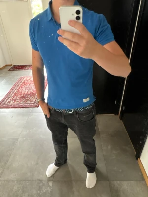 Blå pikétröja med krage - Säljer en klassisk blå pikétröja med krage och två knappar framtill. Tröjan har korta ärmar och sitter väldigt bra kring axlarna och bröstet.