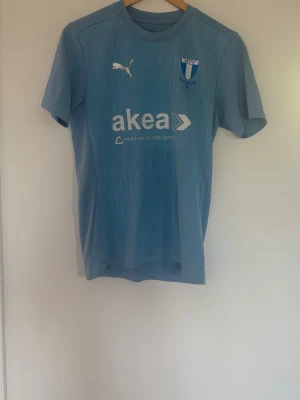Ljusblå Malmö FF matchtröja Puma - Säljer en ljusblå Malmö FF matchtröja från Puma med klubbmärke och sponsortryck på bröstet. Tröjan har korta ärmar och rund hals, tillverkad i ett lätt och funktionellt material som passar perfekt till träning eller match.