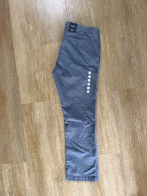 Grå chinos med rak passform - Snygga grå chinos med rak passform och klassiska detaljer som bälteshällor och bakficka med knapp. Tillverkade i ett mjukt och lätt material som passar perfekt till vardagslooken. Enkla att matcha med både skjorta och t-shirt.