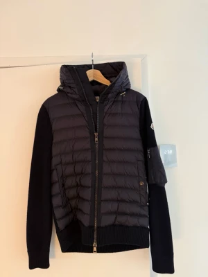 Moncler cardigan | storlek small - Säljer en väldigt fin Moncler cardigan/jacka i mörk marinblå färg, storlek 3.  Modellen kombinerar stickade ärmar och rygg med vadderad dunfront och huva. Moncler-logotyp på ärmen samt ficka med dragkedja. En snygg och användbar modell som fungerar perfekt under höst, vår och mildare vinterdagar.  Mycket sparsamt använd och väl omhändertagen. Inga hål, revor eller andra skador. 