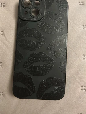 Svart mobilskal med läppar - Snyggt svart mobilskal med upphöjda läppmönster över hela baksidan. Skalet har en matt finish och är gjort i tåligt plastmaterial. Passar perfekt för dig som vill ha en unik och trendig look på mobilen.