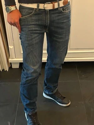 Mörkblå jeans regular fit - Säljer ett par mörkblå jeans med regular fit och klassisk femficksdesign. Jeansen har subtila slitningar och kontrastsömmar för en avslappnad look. Tillverkade i denim och bälteshällor. Perfekta till sneakers och vardagsstil. (Liten defekt på ena benet som visas på sista sida men inget märkvärdigt)