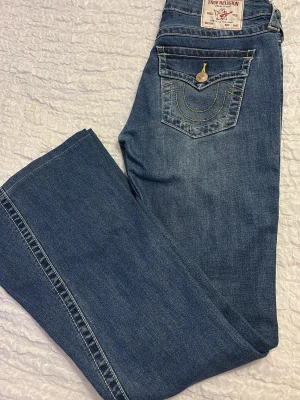 Blå True Religion bootcut jeans - Säljer ett par blå bootcut jeans från True Religion med klassiska kontrastsömmar och snygga detaljer på bakfickorna. 