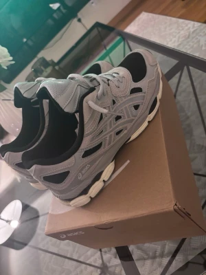 Grå och svarta Asics sneakers - Snygga sneakers från Asics i grått och svart med mesh och mockadetaljer. Skorna har en chunky sula i vitt och grått samt klassiska Asics-loggor på sidan. Perfekta för en sportig och trendig look.