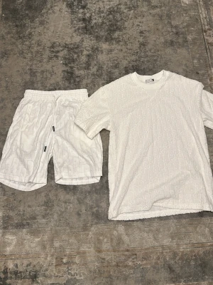 Vitt set med strukturmönster - Säljer ett vitt set med t-shirt och shorts i matchande strukturmönster. Setet har en avslappnad passform och är tillverkat i ett mjukt material med diskret mönster över hela ytan. Perfekt för dig som gillar stilrena och bekväma plagg.