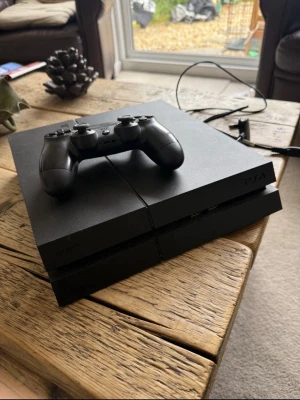 PlayStation 4 med handkontroll - Säljer en svart PlayStation 4 med tillhörande svart DualShock 4-handkontroll. Konsolen har en stilren, kantig design i matt plast och passar perfekt för gaming och streaming. Strömkabel och HDMI-kabel medföljer.