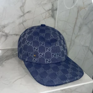 Blå mönstrad keps - Säljer en blå keps med det klassiska monogrammet över hela kepsen. Kepsen har böjd skärm och är tillverkad i ett denimliknande material. Perfekt för dig som vill ha en stilren och lyxig accessoar.