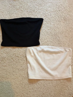 Svart och vit bandeau tubtopp - Två bandeau tubtoppar i svart och vitt. Båda är ribbade och ärmlösa, perfekta för sommaren. Snygga att styla med jeans eller kjol för en enkel och trendig look. Skriv pm vid funderingar!☺️