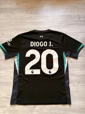 Diogo Jota tröja - Liverpool FC matchtröja – Diogo J. #20  Säljer en svart Liverpool FC-tröja med Diogo J. #20 på ryggen. Tröjan har Liverpool-emblem och Standard Chartered som huvudsponsor samt Expedia på ärmen.  Detaljer:  * Liverpool FC * Svart bortatröja * Diogo J. #20 * Premier League-logga på numret * Storlek: S (enligt etiketten) * Bra skick överlag