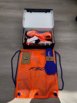 Adidas F50 orange fotbollsskor - Säljer ett par grymma Adidas F50 fotbollsskor i orange med blå detaljer. Skorna har snörning, låg profil och lätta material för maxad speed. Medföljer blå innersulor, skopåsse och extra dobbar. Perfekta för dig som vill dominera på planen.