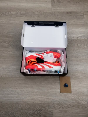 Adidas vita och röda predators fotbollsskor - Säljer ett par grymma Adidas fotbollsskor i vitt och rött med blå dobbar. Skorna har en modern, strömlinjeformad design och är tillverkade i syntetmaterial för bästa prestanda på planen. Perfekta för dig som vill sticka ut och få bra grepp på gräs.