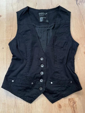 Y2K svart corset/vest – S - Snygg svart Y2K-inspirerad corset/vest med silverfärgade knappar, fickdetaljer och justerbart spänne baktill 🖤✨ Perfekt till low waist-jeans eller kjol för en riktigt cool 00-talslook!  🤎 BUDAS UT PÅ LIVE! 🤎 Denna topp kommer att budas ut på min Plick Live 25 augusti kl. 19:00! 🛍️✨
