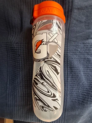 Gatorade GX vattenflaska orange lock - Säljer en Gatorade GX vattenflaska med svartvitt marmormönster och stort Gatorade-tryck. Flaskan har ett orange lock med smart öppning och inbyggd sil. Perfekt för träning eller vardagsbruk, rymmer mycket vätska och är lätt att bära med sig.