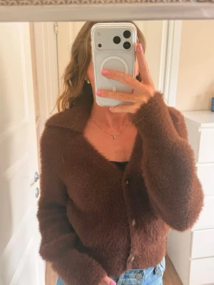 Brun fluffig Adoore-kofta med krage - Mysig brun kofta med fluffig textur och krage. Koftan har knappar framtill och långa ärmar, perfekt att slänga över en topp. Passar till jeans för en avslappnad look.