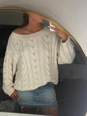 Offwhite kabelstickad tröja - Säljer en oversized offwhite kabelstickad tröja med bred ribbad halsringning som kan bäras off shoulder. Tröjan har långa ärmar och ett klassiskt flätmönster. Perfekt att styla med jeans eller kjol för en chill look.