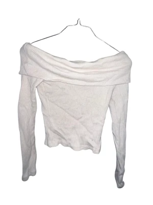 Vit offshoulder ribbad topp - Trendig vit offshoulder topp med långa ärmar och ribbad struktur. Perfekt för dig som vill ha en stilren och modern look. Toppen är figurnära och har en bred krage som vilar snyggt över axlarna. Passar jättebra till allt. 