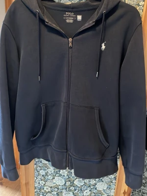 Svart hoodie från Polo Ralph Lauren - Klassisk svart hoodie från Polo Ralph Lauren med dragkedja framtill, huva med snörning och två fickor. Ikoniska loggan broderad på bröstet. Perfekt för en avslappnad och stilren look. Nästintill nyskick. Köpt i Ralph lauren butik i usa. Pris kan diskuteras vid snabb affär