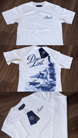 Vit t-shirt med blått tryck Marcel - Vit t-shirt med blått tryck från Marcel. Framsidan har en liten logga på bröstet och baksidan har ett stort motiv med vinflaska, glas och texten 'Dos Lith'. Klassisk passform och rund hals. Perfekt för dig som gillar stilrena men ändå unika plagg.