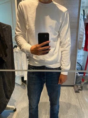 Vit basic sweatshirt - En stilren vit sweatshirt med rund hals och långa ärmar. Tröjan har ribbade muddar vid ärmslut och nederkant, perfekt för en clean och enkel look. Tillverkad i mjukt material som känns skönt mot huden.