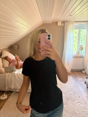 Svart basic t-shirt i bomull - En enkel svart t-shirt med rund hals och korta ärmar. Tillverkad i mjuk bomull och har en normal passform som sitter snyggt till jeans eller shorts. Perfekt för en clean och avslappnad stil.