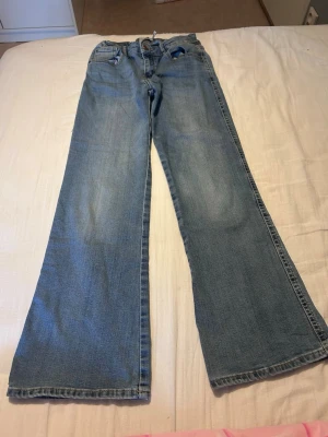 Ljusblå utsvängda jeans - Säljer ett par ljusblå jeans med utsvängda ben och klassisk femficksdesign. Jeansen har låg midja och är perfekta för dig som gillar en avslappnad och trendig look. Passar dig som vill ha ett par snygga och bekväma jeans till vardags.
