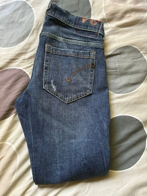 Blå slitna jeans med raka ben - Säljer ett par blå dondup jeans med raka ben och slitningar på både lår och knän. Jeansen har klassisk femficksdesign och kontrastsömmar. Perfekta för dig som gillar en avslappnad och trendig look. W30 L30