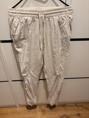 Beiga linnebyxor från H&M - Säljer ett par beiga linnebyxor från H&M i storlek XS. Byxorna har resårmidja med dragsko och sidofickor. Tillverkade i en luftig linnemix som är perfekt för varma dagar. Avslappnad passform och raka ben.