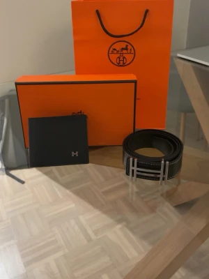 H bälte och plånbok - Snyggt svart skärp i skinn med silverfärgat H-spänne och vita kontrastsömmar. Perfekt accessoar för att lyfta din outfit med en stilren och exklusiv touch.