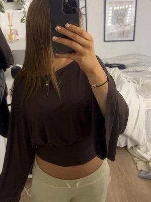 Brun croppad topp med vida ärmar - Säljer en brun croppad topp med bred midjeresår och vida, fladdriga ärmar. Materialet känns mjukt och följsamt mot huden. Storleken på toppen är S💕
