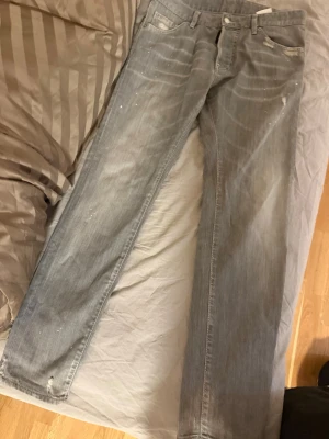 Gråa raka jeans från Dsquared2 äkta - Säljer ett par gråa jeans från Dsquared2 med raka ben och slitna detaljer. Jeansen har klassisk femficksmodell, knappgylf och är tillverkade i bomull. Perfekta för en avslappnad och trendig look.