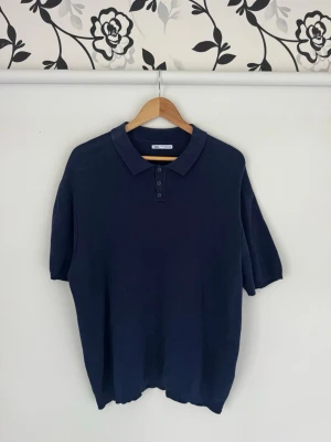 Mörkblå ribbad pikétröja Zara XL - Mörkblå pikétröja från Zara i ribbat material med klassisk krage och tre knappar framtill. Tröjan har korta ärmar och en enkel, stilren design som funkar till många olika looks. Nypris: 799:-